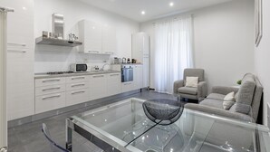 Una cocina moderna con armarios blancos, una mesa de comedor de vidrio y un sofá gris en una sala de estar.