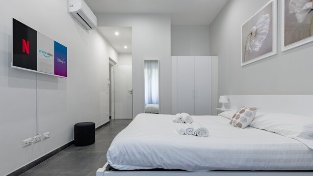 Una habitación de hotel moderna con una cama grande, un televisor de pantalla plana en la pared y un ventanal con cortinas.