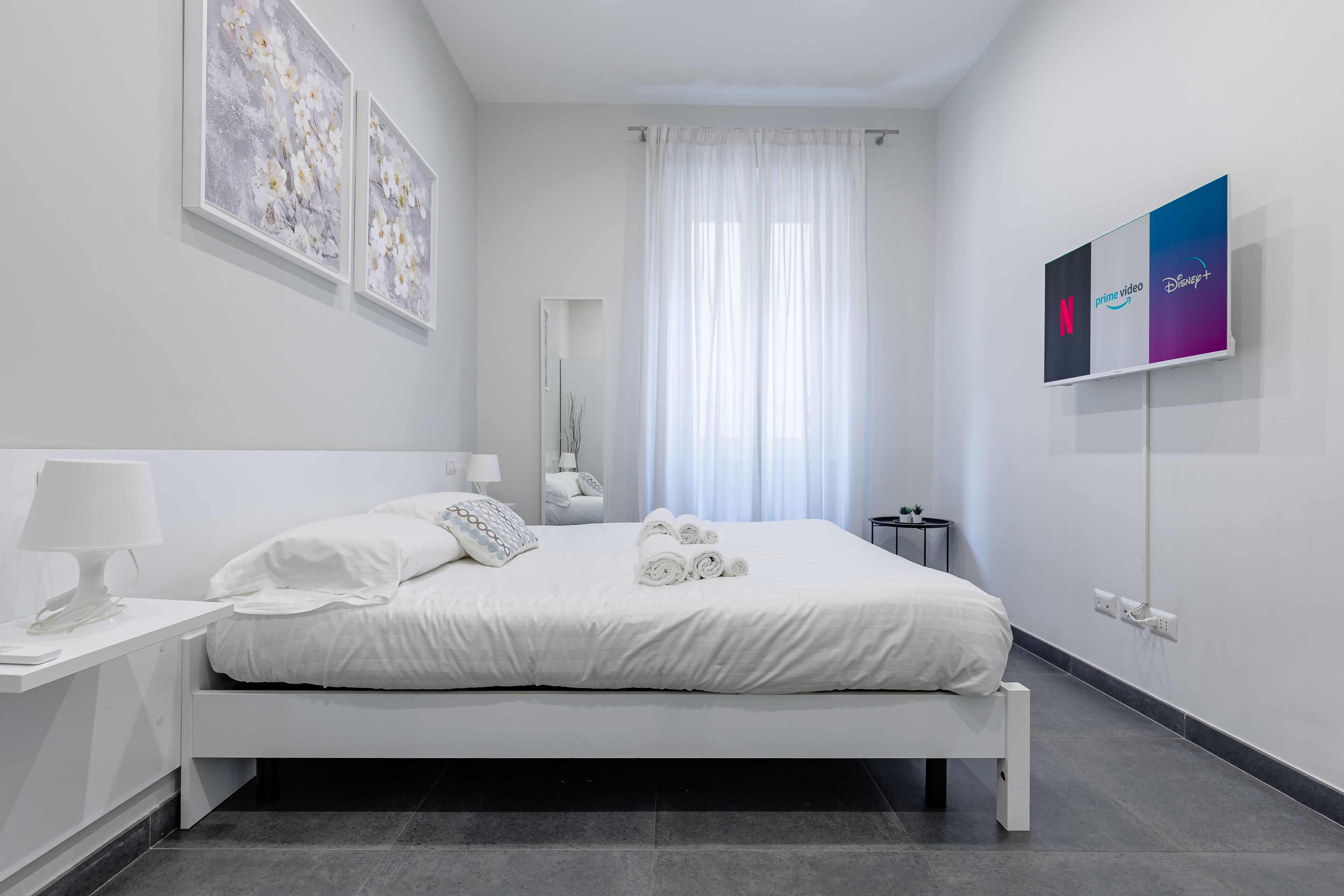 Une chambre à coucher moderne avec un lit, des tables de chevet, une commode, un miroir et des œuvres d’art accrochées au mur.