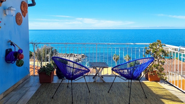 A balcony with two blue chairs, a small table, and a view of the sea. - Casa Azzurra (Pizzo)