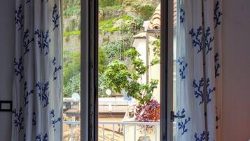 Ein Schlafzimmer mit Bett, einem Fenster mit Vorhängen und Blick auf einen Garten sowie Gebäude im Freien.