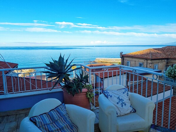 A balcony with two white chairs and a potted plant, overlooking a coastal view with a clear sky. - Casa Azzurra (Pizzo)
