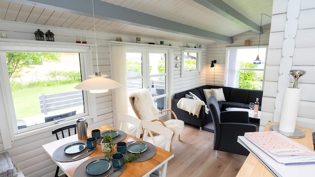 Interior acogedor de una cabaña con comedor, sofá y ventana con vistas a un espacio verde.