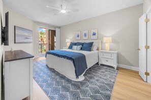 Une chambre à coucher avec un lit, des tables de chevet, un ventilateur de plafond et une vue sur l’extérieur.