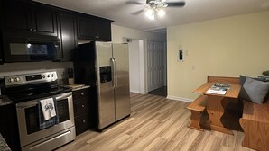 A modern kitchen with dark cabinets, stainless steel appliances, and a wooden dining table.