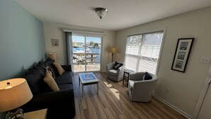 A living room with a sofa, armchairs, a coffee table, and a view of a marina through large windows.