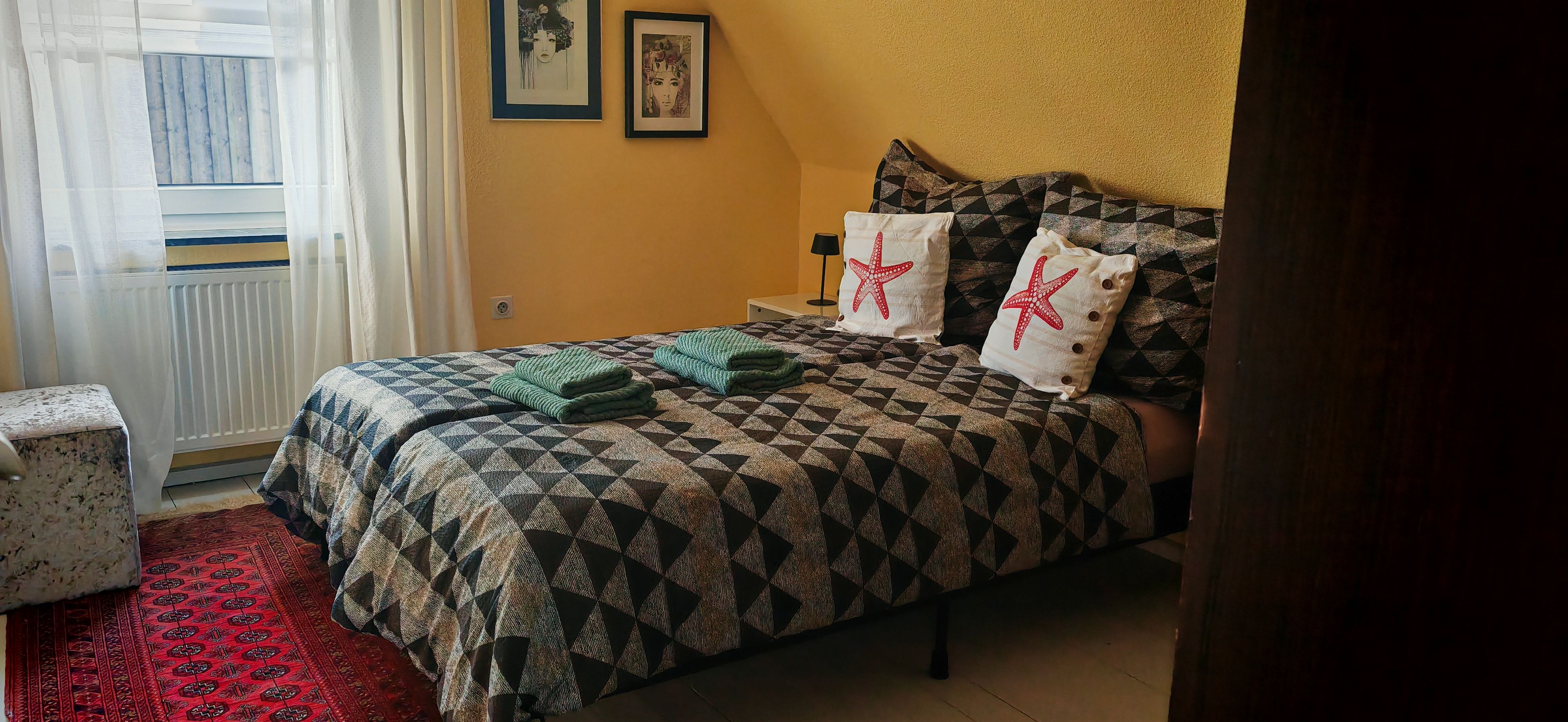 A bedroom with a bed, pillows, a nightstand, a lamp, and a window with curtains.