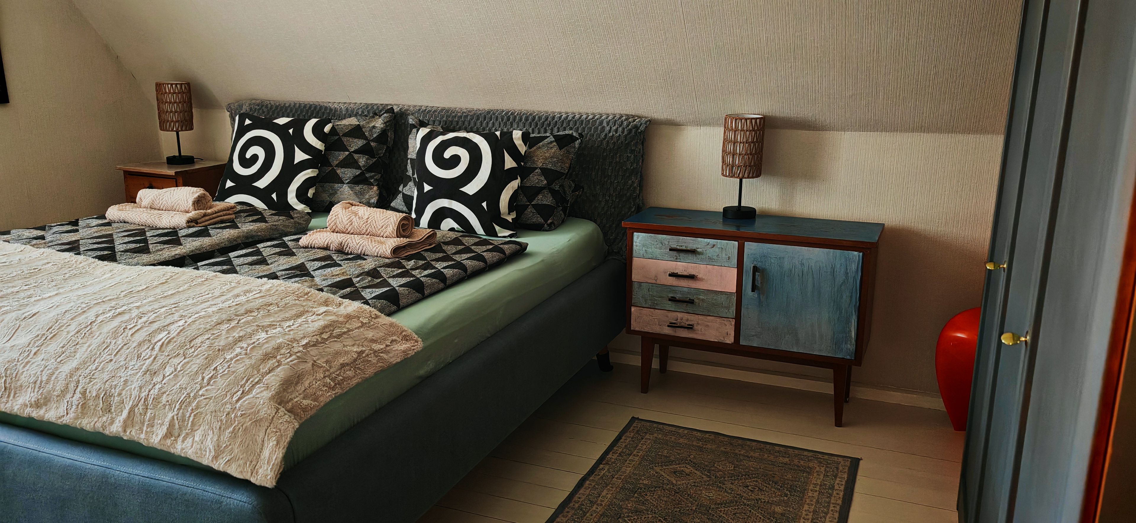 Une chambre à coucher avec un lit, une table de chevet, une commode et une porte.