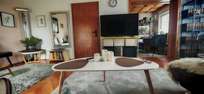 A living room with a TV, a dining table with candles, a bookshelf, and a large window. - Ferienhaus Villa Zauberblick am Rennsteig Frankenwald. Pets welcome! (Ludwigsstadt)
