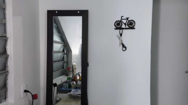 Un couloir étroit, orné d’un miroir qui reflète une pièce où l’on aperçoit un lit et une décoration murale représentant un vélo.