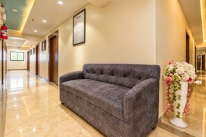 A hallway with a grey sofa, a framed sign on the wall, and a floral arrangement. - Glitz Saineel Executive Near Juhu Beach (Mumbai)