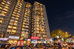 A high-rise building with multiple balconies, various shops, and a busy street with vehicles and pedestrians. - Glitz Saineel Executive Near Juhu Beach (Mumbai)