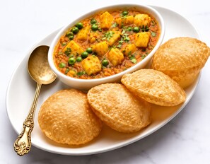 Un bol de curry aux pommes de terre et aux petits pois, accompagné de trois petits pains ronds et dorés, servis sur une assiette blanche.