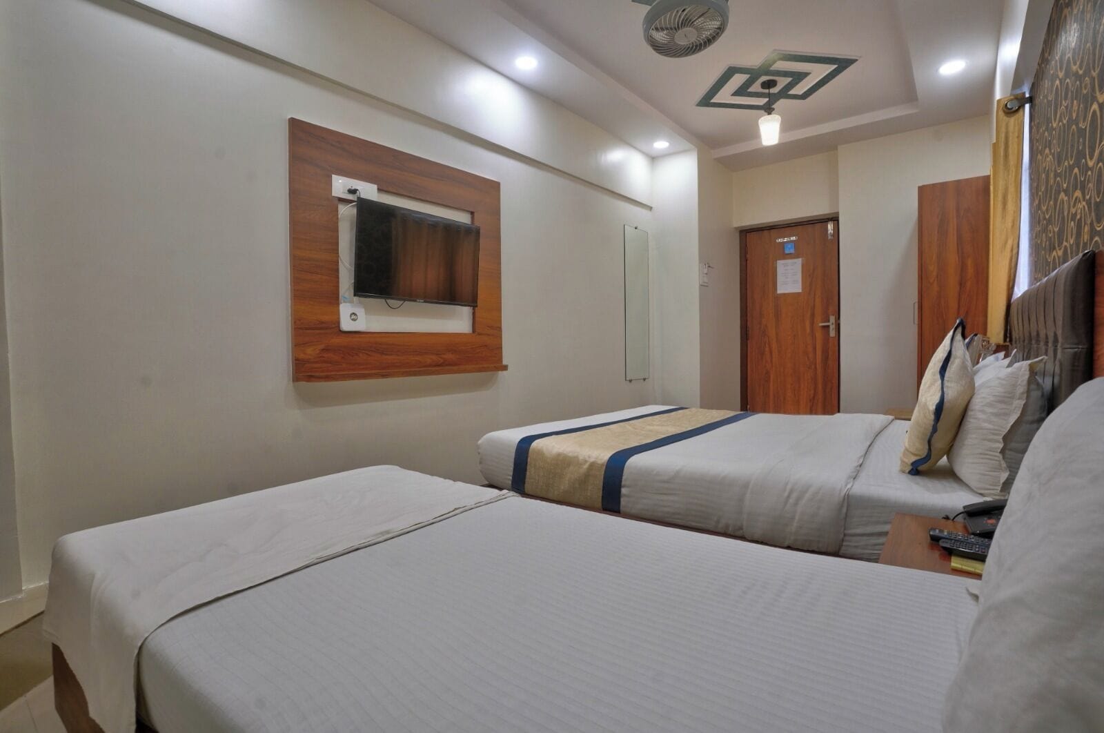 A hotel room with two beds, a television mounted on the wall, and a wooden door.