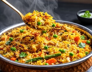 A bowl of biryani with visible ingredients like peas, carrots, and meat. - Glitz Saineel Executive Near Juhu Beach (Mumbai)
