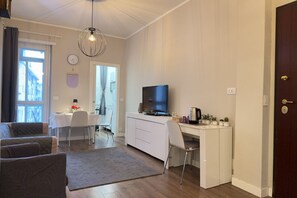 Ein kompakter Wohnraum mit Essbereich, einem Fernseher, einem Schreibtisch mit Computer und einer Couch.