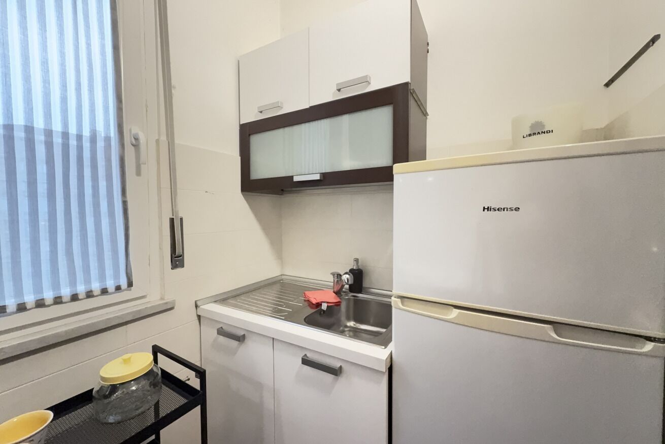 A compact kitchen with a stainless steel refrigerator, a sink, and a window with blinds.