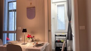 Een eetgedeelte met een tafel gedekt voor twee personen, een wandklok, een agenda en een raam met gordijnen.
