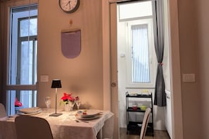 Ein Essbereich mit einem Tisch für zwei Personen, einer Wanduhr, einem Kalender und einem Fenster mit Vorhängen.