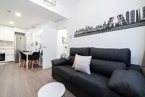 A modern living room with a black sofa, a small round table, and a dining area with a white table and chairs. - Comfortable apartment for families and business travelers   (Getafe)