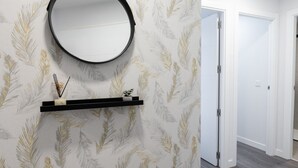 Un interior moderno con un espejo montado en la pared, una estantería con objetos decorativos y un papel pintado estampado.