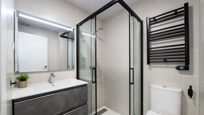 Un baño moderno con cabina de ducha de vidrio, inodoro blanco, tocador con espejo y barra para toallas.