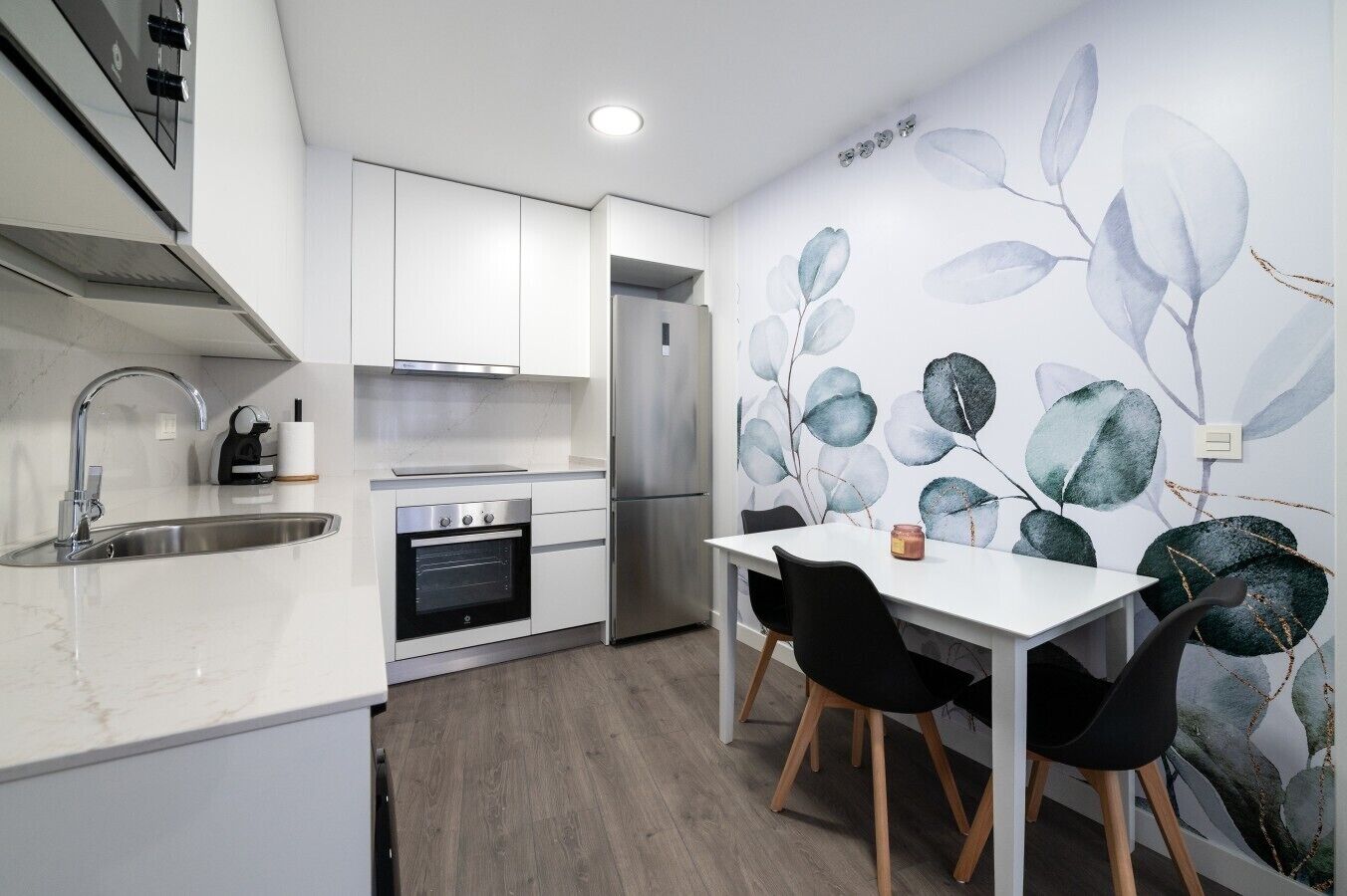 A modern kitchen with white cabinetry, a built-in oven, and a stainless steel refrigerator.
