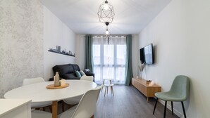 Una sala de estar moderna con comedor, un sofá, un televisor y vistas a través de una ventana.
