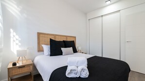 Habitación de hotel con cama, mesita de noche, lámpara, armario y ventana con luz solar.