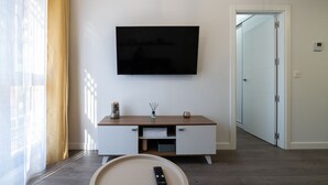 Una sala de estar moderna con un televisor de pantalla plana montado en la pared, una consola de madera con cajones, un control remoto sobre una bandeja y una puerta que da a otra habitación.