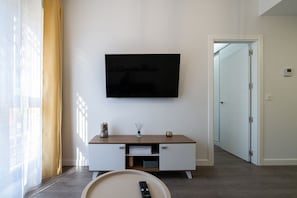 A modern living room with a flat-screen TV mounted on the wall, a wooden console table with drawers, a remote control on a tray, and a door leading to another room. - Modern apartment 20 min from Madrid (Getafe)