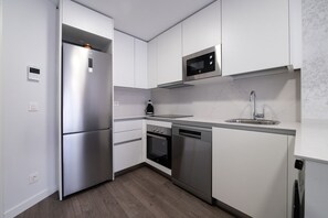 Une cuisine moderne dotée d’appareils électroménagers en acier inoxydable, de meubles blancs et d’un four à micro-ondes encastré.