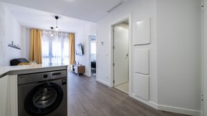 Una cocina moderna con lavadora, un comedor con cortinas amarillas y un pasillo que conduce a un dormitorio.