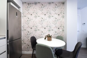 A modern kitchen with a stainless steel refrigerator, a round dining table with four chairs, and a floral wallpaper.