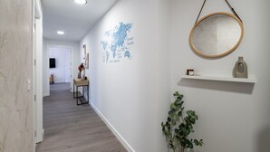 Un pasillo con piso de madera, un mapa en la pared, un espejo redondo, un estante con objetos y una planta en maceta.