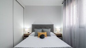 Una habitación de hotel moderna con una cama grande, dos mesitas de noche con lámparas y un cabecero gris.