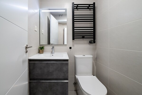 A modern bathroom with a white sink, dark-toned vanity, a toilet, and a towel rack.