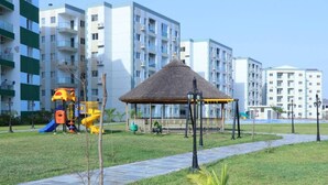 A playground with a slide and climbing structures, a thatched-roof gazebo, and a paved pathway. - Colorful & Modern Escape: Pool, Balcony, Security! (Sakumono)