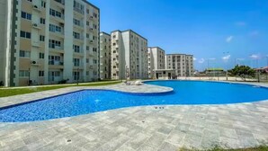 A modern apartment complex with a central swimming pool, surrounded by a paved area and greenery. - Colorful & Modern Escape: Pool, Balcony, Security! (Sakumono)