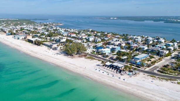 An aerial view of a coastal residential area with houses, a beach, and a marina. - Heavenly Sunset - Private Pool and Putting Green! (Bradenton Beach)