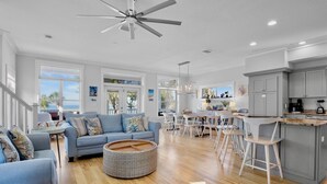 A spacious living area with a blue sofa, a round wicker coffee table, and a kitchen area with a bar counter and stools. - Heavenly Sunset - Private Pool and Putting Green! (Bradenton Beach)