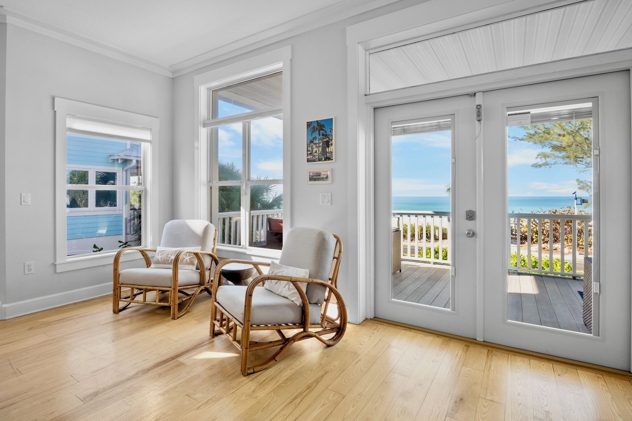 A bright room with large windows, a wicker chair, and a view of the ocean.