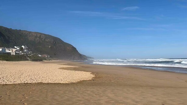 A beach with a sandy shore, a cliff with buildings, and waves in the background. - Lovely flat, walk to Glentana beach... Play golf! (Great Brak River)