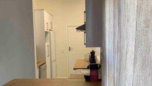 A compact kitchen with a wooden table, two bar stools, a refrigerator, and a coffee machine. - Lovely flat, walk to Glentana beach... Play golf! (Great Brak River)