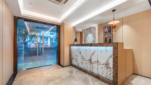 A modern reception area with a marble reception desk, glass doors leading outside, and a ceiling with recessed lighting. - Yueduo Selected Hotels (Guangzhou)