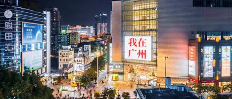 A cityscape at night with illuminated buildings, a prominent sign reading 'I am in Guangzhou,' and a busy street with pedestrians and vehicles.