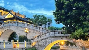 A stone bridge over a calm river with a reflection of the bridge and lights, surrounded by trees and buildings. - Yueduo Selected Hotels (Guangzhou)