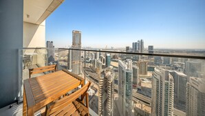A balcony with a wooden table and chairs, overlooking a cityscape with high-rise buildings. - Downtown Dubai Chic 1BR Retreat (Dubai)