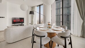 A modern living room with a round dining table set for four, a sofa, and a TV displaying 'NETFLIX'. - Stylish 2BR + Maid’s Apartment in Sobha Hartland (Dubai)