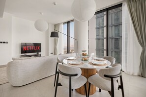 Ein modernes Wohnzimmer mit einem runden Esstisch, gedeckt für vier Personen, einer Couch und einem Fernseher, der 'NETFLIX' anzeigt.